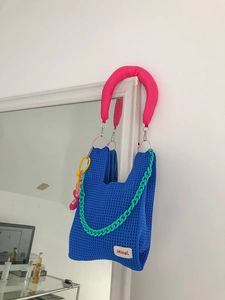 Detail of blue knitted tote bag with pink padded handle and mint green plastic chain