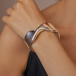 Macro shot of silver-tone polished metal wide cuff bracelet with artistic wavy texture