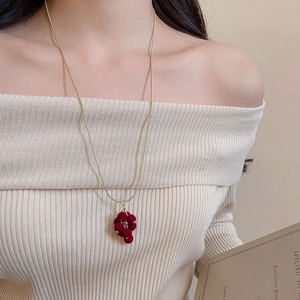 Close-up of a vintage-style gold necklace with a dark red flocked grape tassel pendant
