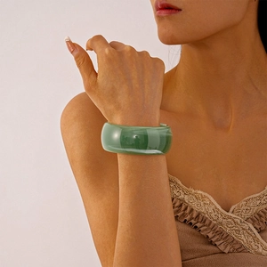 Close-up of a wide green resin bangle with vintage striped texture on a model wrist