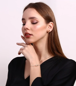 Detail of model wearing a gold bow pendant bracelet and matching crystal stud earrings