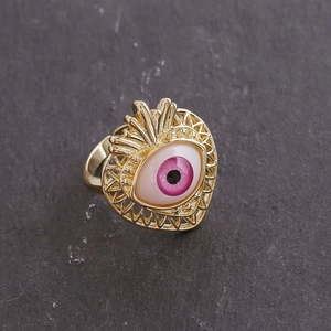 Macro detail of 18K gold evil eye ring with pink iris on dark stone background texture