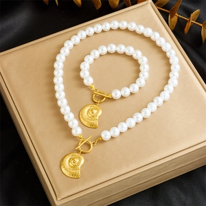 Detail of pearl jewelry set with gold nautilus pendants on black silk background