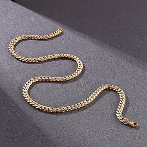 Close-up of a high-polish gold Cuban link chain with a secure lobster clasp on grey texture