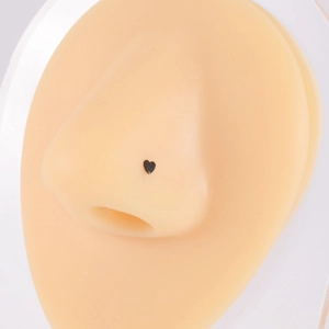 Primo piano di un piercing al naso a forma di cuore scuro su un modello di naso vero