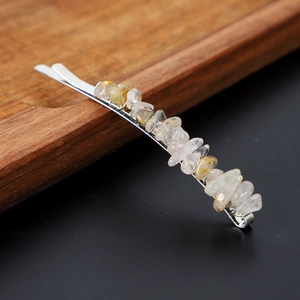 Detailed view of natural crystal stones on a silver metal hairpin against a dark wood background