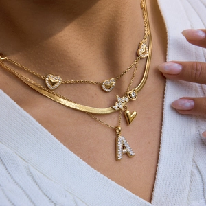 Nahaufnahme mehrlagiger Goldketten mit Herzanhängern und A-Anhänger aus Strass für Damen