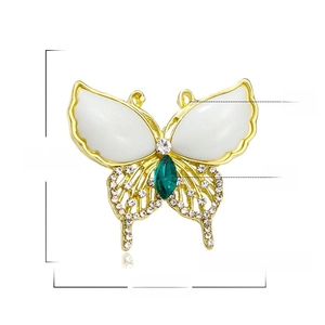 Detailed view of golden butterfly brooch with white resin wings and green stone, 4x3.7cm