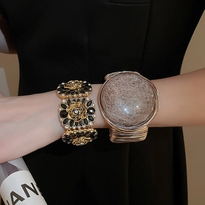 Close-up of stacked gold floral bracelets with rhinestones and vintage textured charm