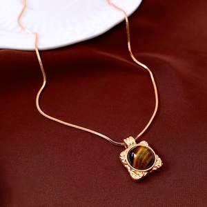 Dettaglio collana placcata oro 18K con ciondolo tondo in occhio di tigre su tessuto marrone