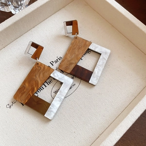Detailed close-up of acrylic geometric drop earrings with brown tortoiseshell and marble patterns