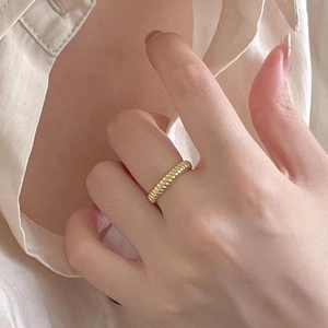 Close-up of a gold twisted croissant ring worn on a finger with warm aesthetic tones