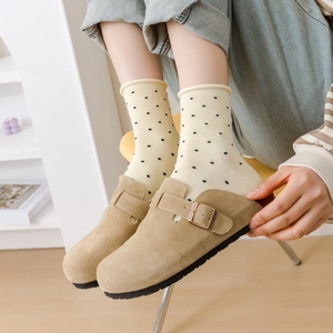 Détail de sabots en daim kaki avec chaussettes mi-hautes en coton crème à pois noirs