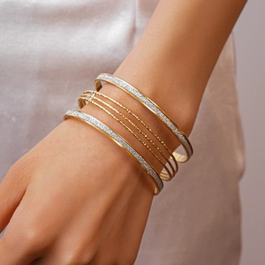 On-model view of multilayer gold bangles with textured silver glitter and polished finish