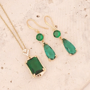 Elegant gold necklace and earring set featuring emerald green stones on textured stone background