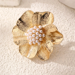 Macro detail of golden flower ring with brushed metal petals and white faux pearls