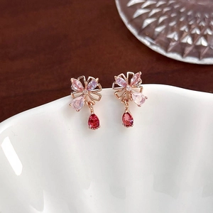Close-up of rose gold flower earring with a deep red teardrop crystal on ceramic