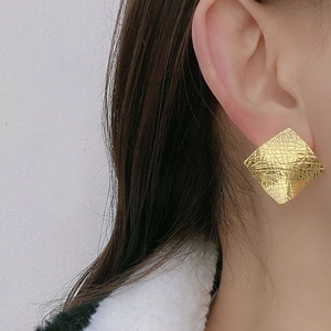 Detailed view of oversized square gold earrings with cross-hatch texture on a model