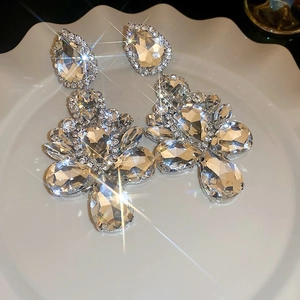 Macro shot of silver teardrop earrings with crystal stones on a white ceramic plate