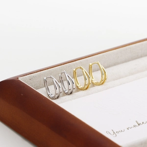 Macro view of gold and silver U-shaped double-line hoop earrings on a linen jewelry box