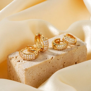 Two pairs of C-shaped gold hoop earrings with zircon stones on beige stone and silk
