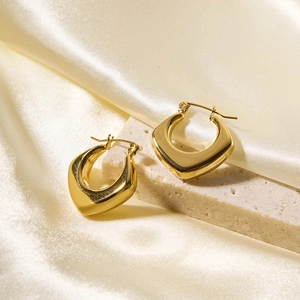 Detailed close-up of golden geometric rhombus hoop earrings on beige silk background