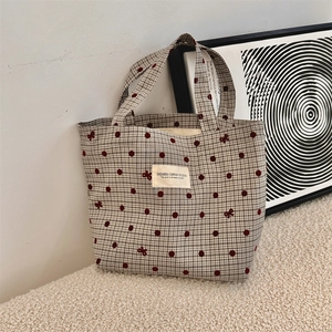 Close-up of canvas tote bag with red polka dots and bow patterns on cream carpet