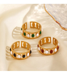 Close-up of three gold adjustable rings with white, green, and black enamel on silk fabric