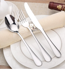 Close-up of polished stainless steel cutlery set on white plate with napkin