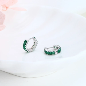 Detail of silver huggie earrings with rectangular green zircons on a ceramic plate