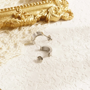 Minimalist silver stainless steel C-shaped stud earrings on white lace background