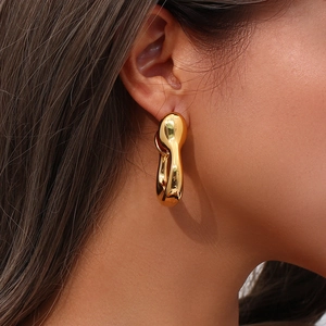 Close-up of model wearing chunky golden hollow sculptural twisted metal hoop earrings
