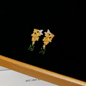Makroaufnahme goldener Blumenohrringe mit grünem Edelstein auf schwarzer Samtbox