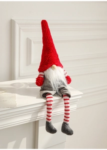 Close-up of a Christmas gnome with long red hat and striped legs sitting on a white mantel