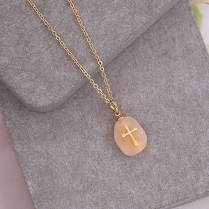 Detail of pink natural stone cross pendant on a thin gold chain against stone