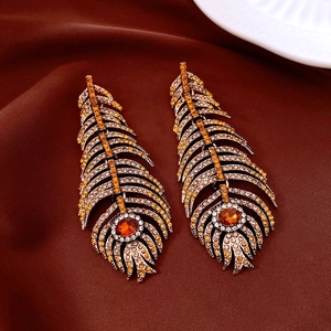 Detailed view of vintage gold feather tassel earrings with amber rhinestones on velvet