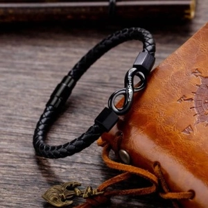Detail of black braided leather bracelet with engraved infinity charm on a notebook