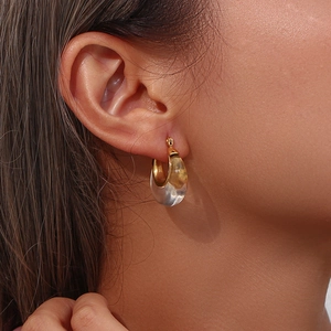Close-up of chunky gold and clear acrylic C-shaped hoop earring worn by a model