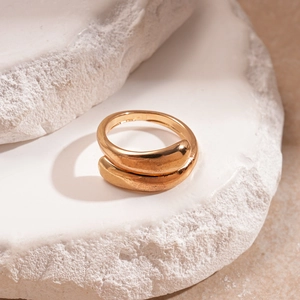 Dettaglio macro di un anello largo dorato lucido su fondo di pietra bianca ruvida
