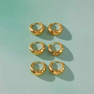 Détail de créoles dorées épaisses avec pierres de zircon gravées en étoile en trois couleurs