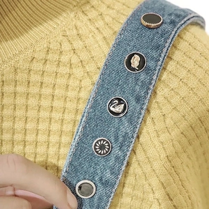 Detailed view of assorted decorative enamel buttons with swan and floral patterns on denim