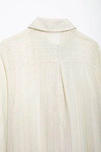 Detail of sheer off-white striped blouse showing back yoke and pleated fabric texture