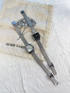 Close-up of square dial watches with silver mesh straps in black and silver finishes