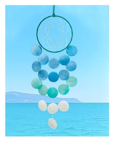 Detail of DIY seashell wind chime with blue gradient discs against ocean and sky background
