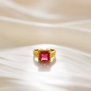 Detail of a gold ring with a square pink gemstone on beige silk fabric background