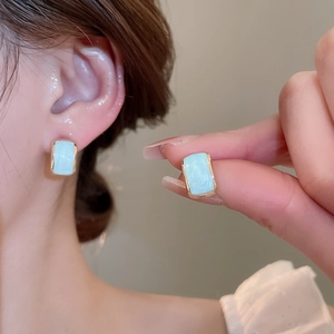 Detail view of gold rectangle earrings with light blue enamel inlay worn by a model