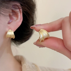 Close-up of matte gold textured round stud earring with shell pattern on a model's ear