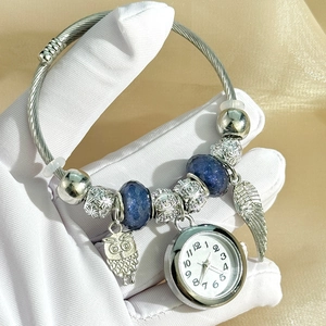 Macro view of silver rope bracelet featuring owl, wing charms and mini watch pendant