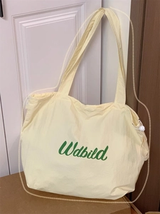 Detail view of a yellow nylon tote bag featuring a green brand logo with drawstring