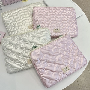 Close-up of quilted laptop sleeve featuring heart and bow patterns with metal zipper